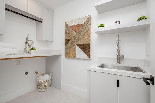A bright and modern laundry room featuring a white sink and white cabinets