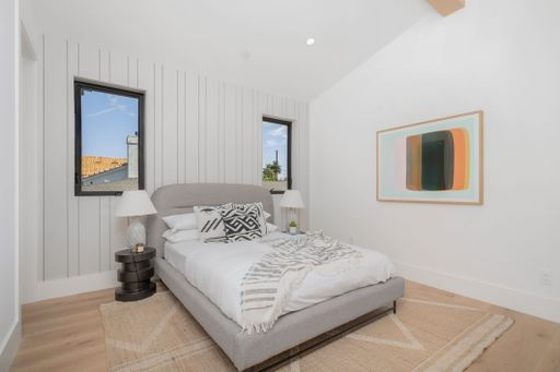 A modern, neutral bedroom featuring a centered double bed with white walls and wooden flooring