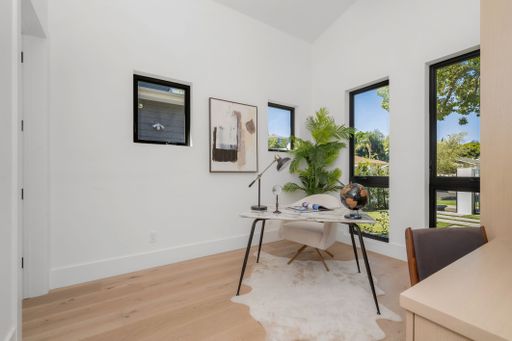 A well-lit home office featuring a tidy desk and chair, with a window on the side providing natural light