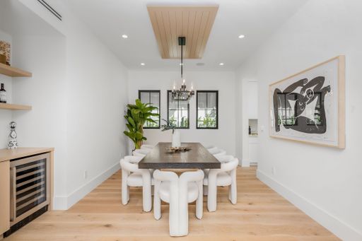A modern white room interior featuring a wooden table and six matching white chairs, arranged in an inviting formation