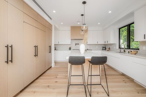 An interior kitchen space, complete with white cabinetry and two bar stools