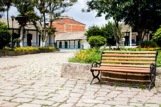 A wooden bench at a park with cobblestone ground