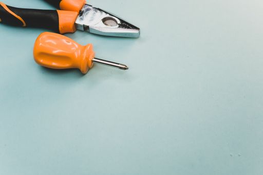 A high angle shot of a small screwdriver and pliers isolated on a light blue background
