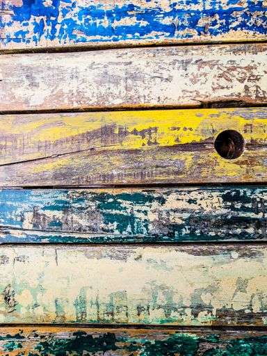 A wooden wall with worn paint of various colors on its planks and a round hole on the side