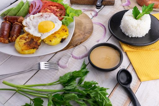 A heavy breakfast spread composed of sunny side up egg, sausages, potato cutlets, fresh salad and rice on a rustic surface