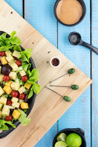 A vertical shot of a platter of fresh salad on a wooden table with food pickers