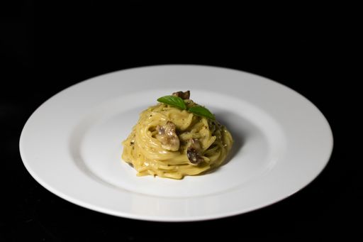 A closeup shot of spaghetti with mushrooms on a white plate isolated on a black background