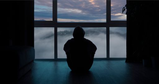 A lonely person from behind sitting near the window and looking at clouded landscape