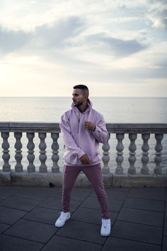 A vertical shot of a young attractive male in a pink street style outfit posing near the sea