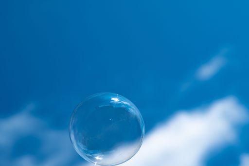 A closeup of a single soap bubble with a cloudy blue sky in the background