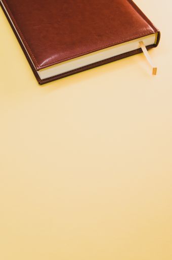 A vertical shot of a brown notebook on pastel yellow background with an empty space for a text