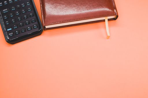 A scientific calculator next to a notebook on pastel peach background