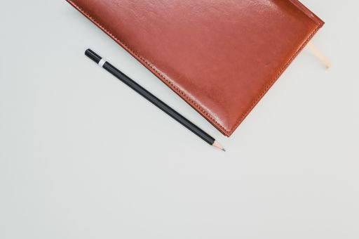 A top view of a notebook next to a pencil on pastel gray background with an empty space for a text