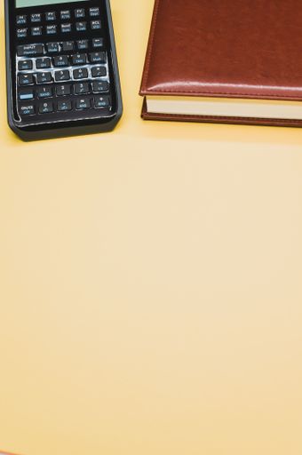 A vertical shot of a scientific calculator next to a notebook on pastel yellow background
