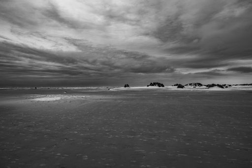A grayscale shot of a sandy beach on a cloudy sky background in Borkum, Germany