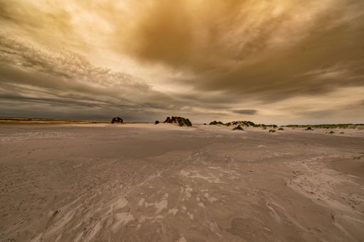 A landscape of the beach covered in the grass under a cloudy sky during a beautiful sunset