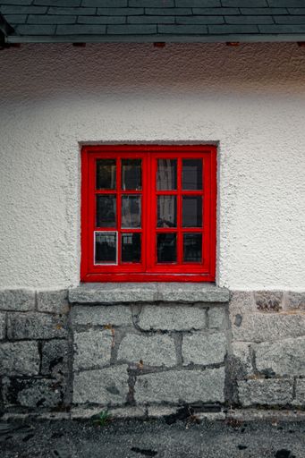 A vertical shot of a red window on a concrete wall