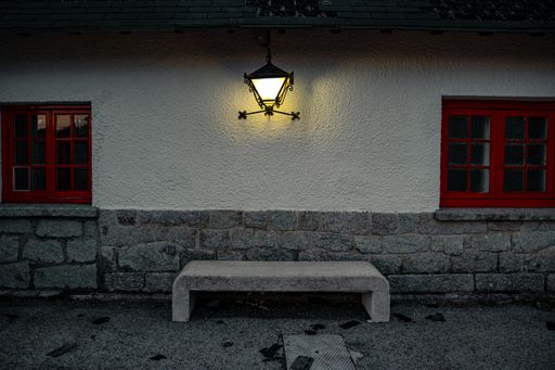 The exterior of a building with red windows and an illuminated lamp hanging over a concrete bench