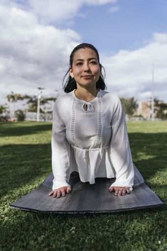 A vertical shot of a Hispanic female doing yoga at a park