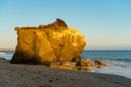 Big rocks in El Matador Beach Malibu with waves washing the coastline during sunset