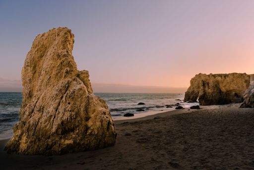 Big rocks in El Matador Beach Malibu with waves washing the coastline during sunset