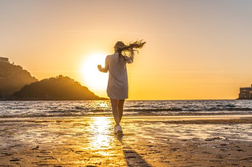 An attractive female standing on the beach at sunset with the sun in the background