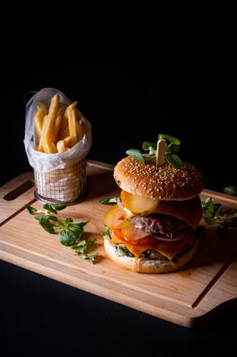 A vertical shot of a delicious burger and french fries on wooden board isolated on black background