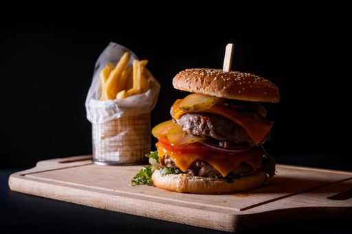 A closeup shot of a double beef burger and french fries on a wooden board on a black background