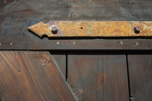 Close-up of an old door with dark brown planks and a part of a rusty old door hinge