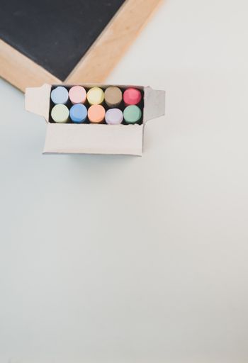 A vertical top-view of a blackboard with colorful chalks on a white surface
