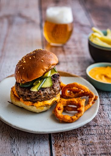 Lamb Burger with spicy onion rings, pickled cucumber and a beer