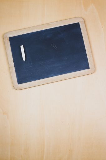 A vertical top view of a blackboard with a chalk on a wooden surface