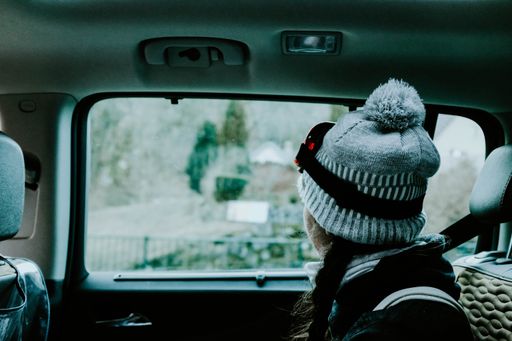 A female with a hat sitting inside a car looking out the window