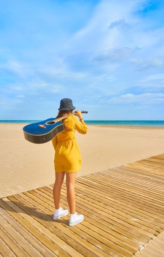A backshot of a Caucasian teenager on the beach holding an acoustic guitar - the concept of fun and leisure