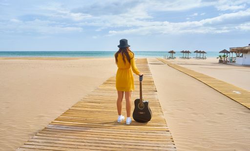 A backshot of a hipster posing with an acoustic guitar on the beach - the concept of fun and leisure