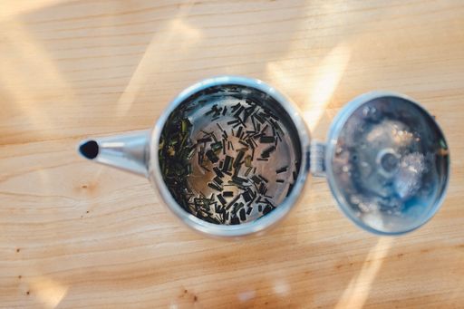 A high shot of a metallic teapot filled with tea on a wooden table under sunlight