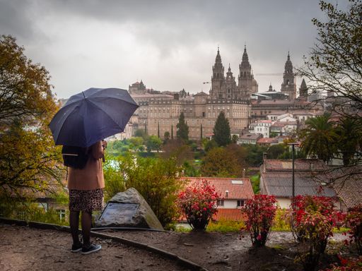A closeup of a female with an umbrella standing and looking at the Cathedral of Santiago de Compostela in Spain on a rainy day