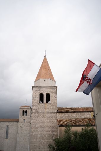 A vertical image of Krk Church with moody weather in daylight
with the Croatian flag in front of it