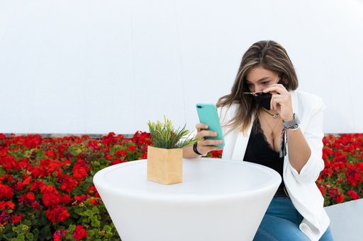 A closeup shot of a young girl using her phone wearing a sanitary mask - concept of the new normal