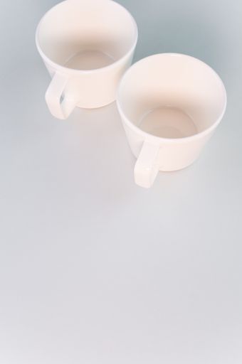 A vertical shot of two empty white coffee cups on a white surface