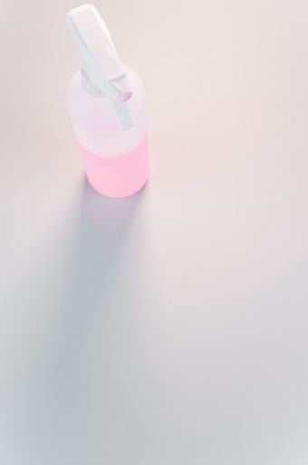 A vertical shot of a spray bottle with pink liquid in it placed on a white surface