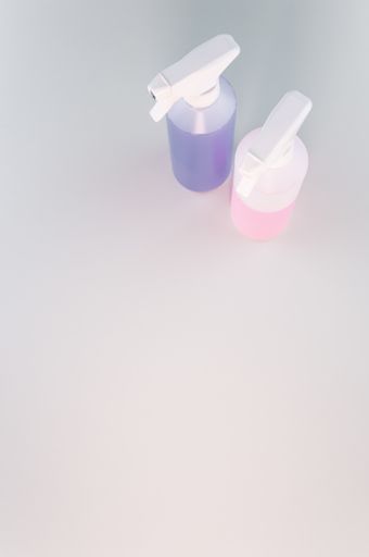 A vertical shot of two spray bottles with pink and purple liquid in them, on a white surface