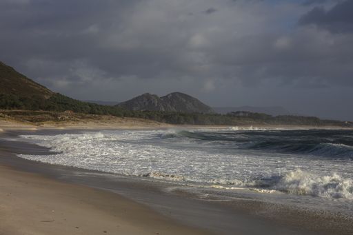 The Larino beach surrounded by hills and greenery under a cloudy sky in Galicia, Spain