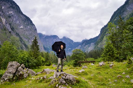 The adventurous hiker standing on the rock with an umbrella and looking at the beautiful mountains