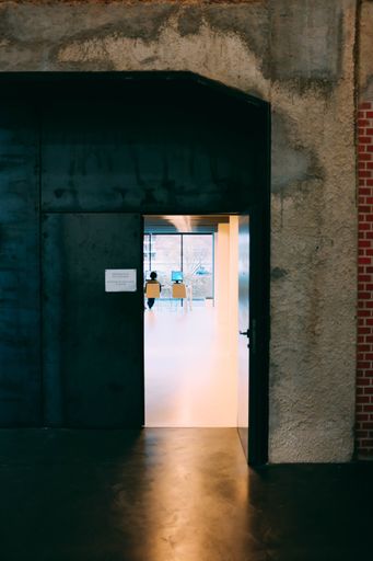 A view of a modern office room with large windows through a metal door under dirty old walls