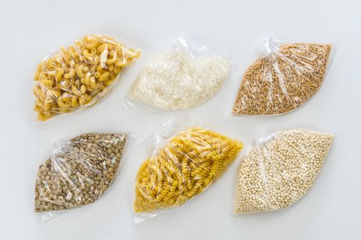 A top view of cellophane bags with various macaronis, rice, and other groceries on white background