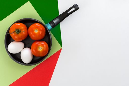 A top view of a pan with three tomatoes and two eggs on a white table with red and green copy text space