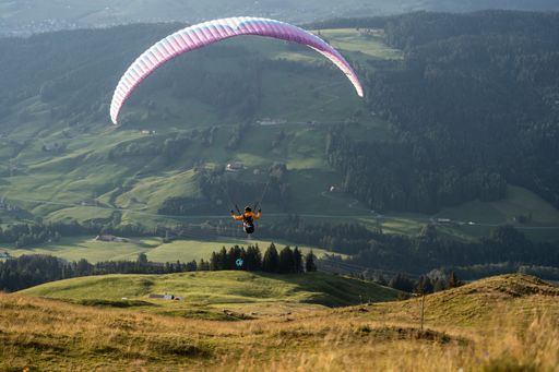 A paraglider in flight, soaring over lush green hills and trees