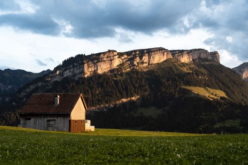 A small cottage in a beautiful green meadow with a majestic mountain range in the background