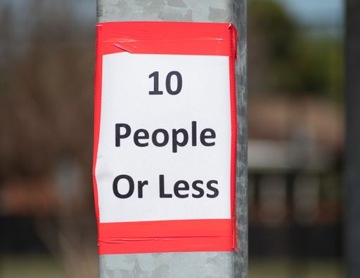 A selective focus shot of a sign that reads 10 People Or Less on a metal pole, the new normal due to COVID-19